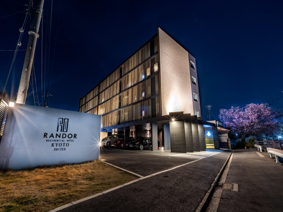 ランドーホテル京都スイーツ — 京都市南区 · 桜の木と並んで建つ夜のレジデンシャルホテル外観