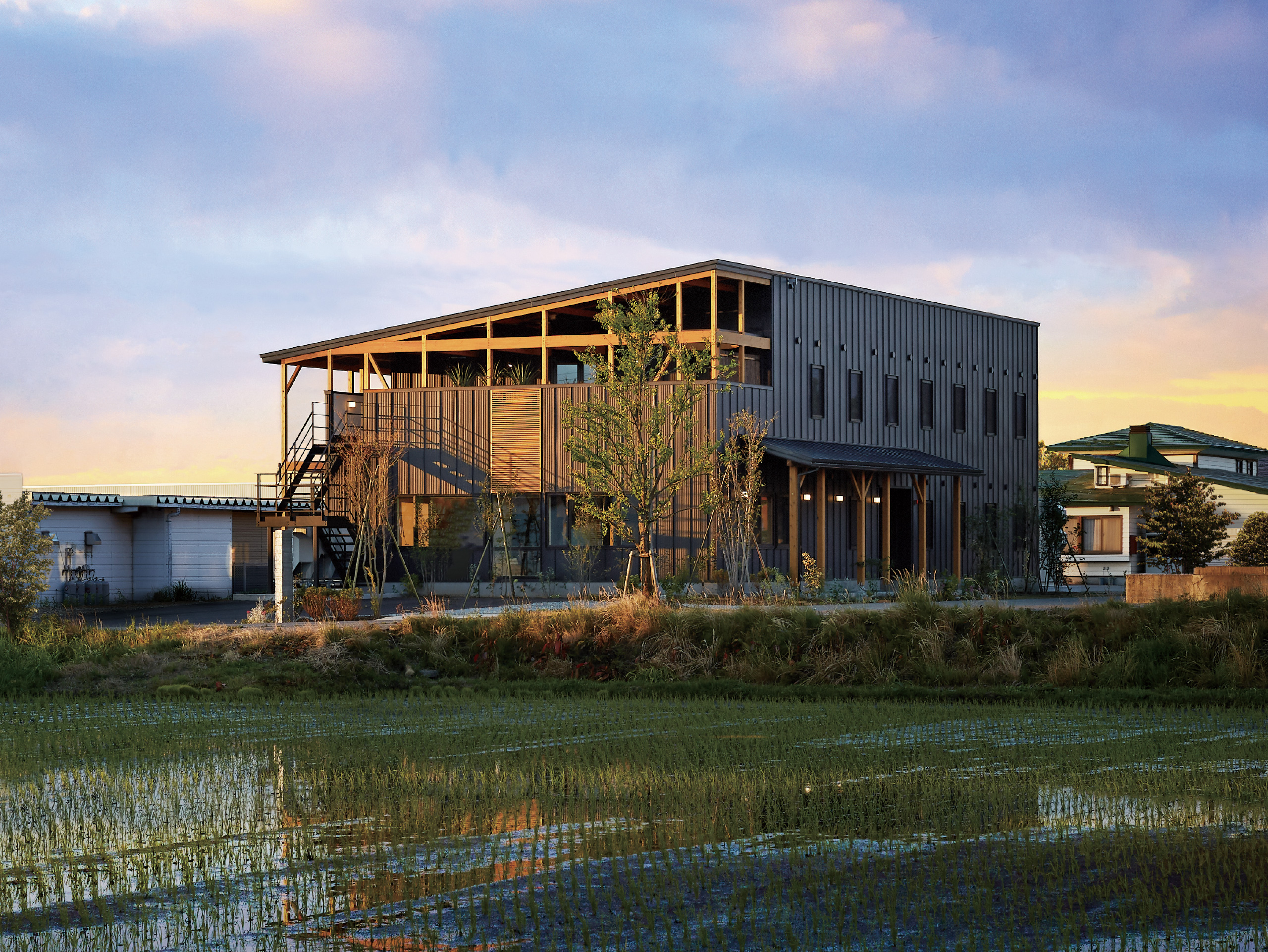 HOTEL SLOW VILLAGE 米沢 — 米沢市春日 · 田園に建つ2022年開業のデザイン一棟宿、夕景が水田に映る外観