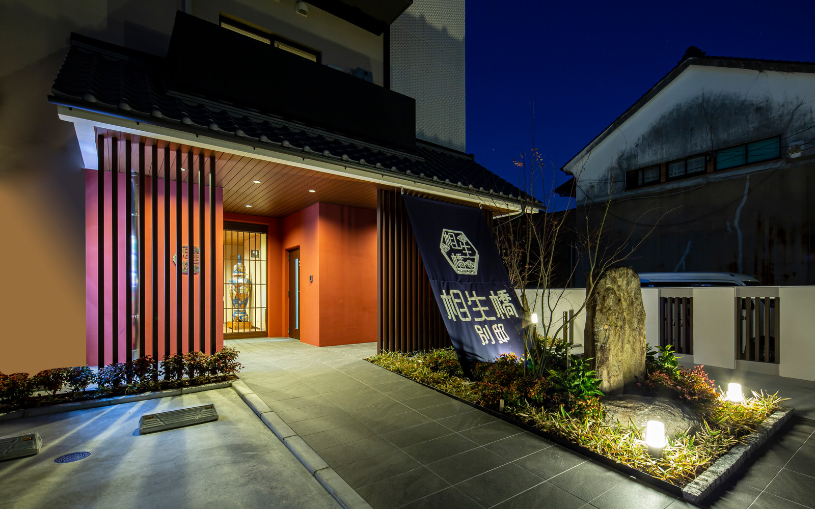 ホテル伊万里 相生橋別邸 — 伊万里・伊万里川沿い · 朱色の外壁と暖簾が映える夕暮れのエントランス