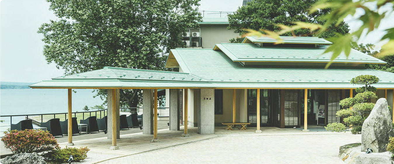 多田屋 — 緑色の瓦屋根と檜柱の玄関棟。七尾湾を背景にした和風建築