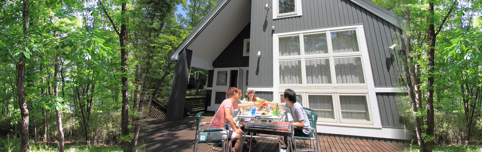 ヴィラージュ那須高原 — 那須町 · 森に囲まれたコテージのデッキで食卓を囲む家族