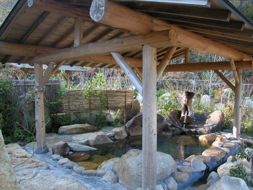 民宿たなべ — 春から秋期に開く木造屋根の露天風呂、石囲みの浴槽と山の緑