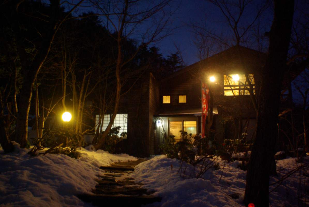 民宿たなべ — 冬の夜、雪の径を照らす玄関灯と暖色の窓明かり、木造二階建て外観