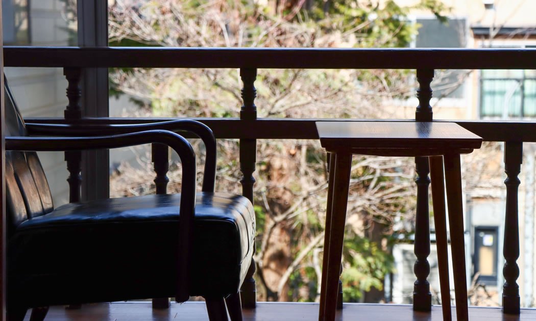 小堀旅館 — 弘前市本町 · 広縁に置かれた古い木椅子と、窓の外に広がる城下町の町並み