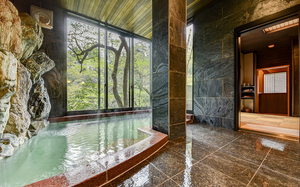 静かな渓谷の隠れ宿 峡泉 — 岩壁をそのまま取り込んだ浴室と、渓谷の樹林に向かって開く大きな窓