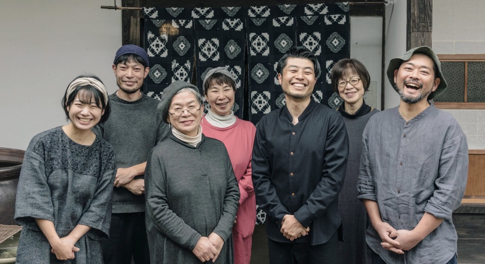他郷阿部家 — 大森町の宿を運営するスタッフ、藍染の暖簾を背にした集合写真