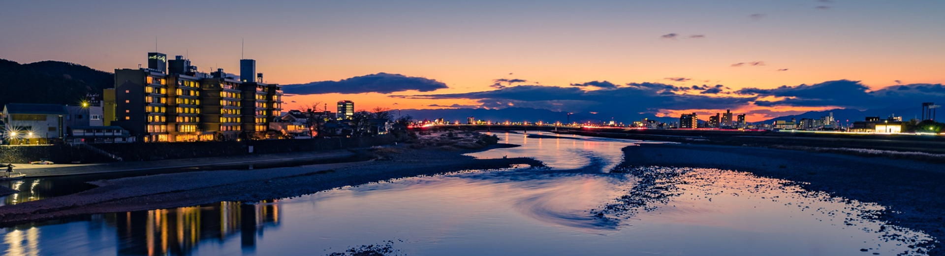十八楼 — 岐阜市湊町・長良川右岸 · 夕暮れの長良川越しに望む外観