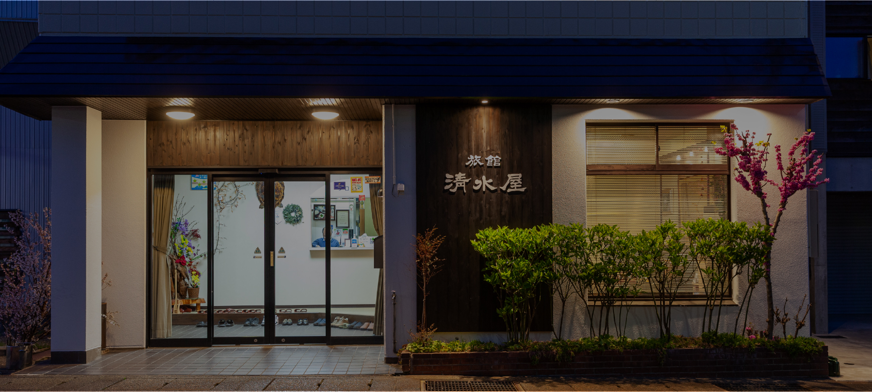 旅館 清水屋 — 新潟県十日町市昭和町 · 夕暮れに灯りのともる玄関まわりと木の看板