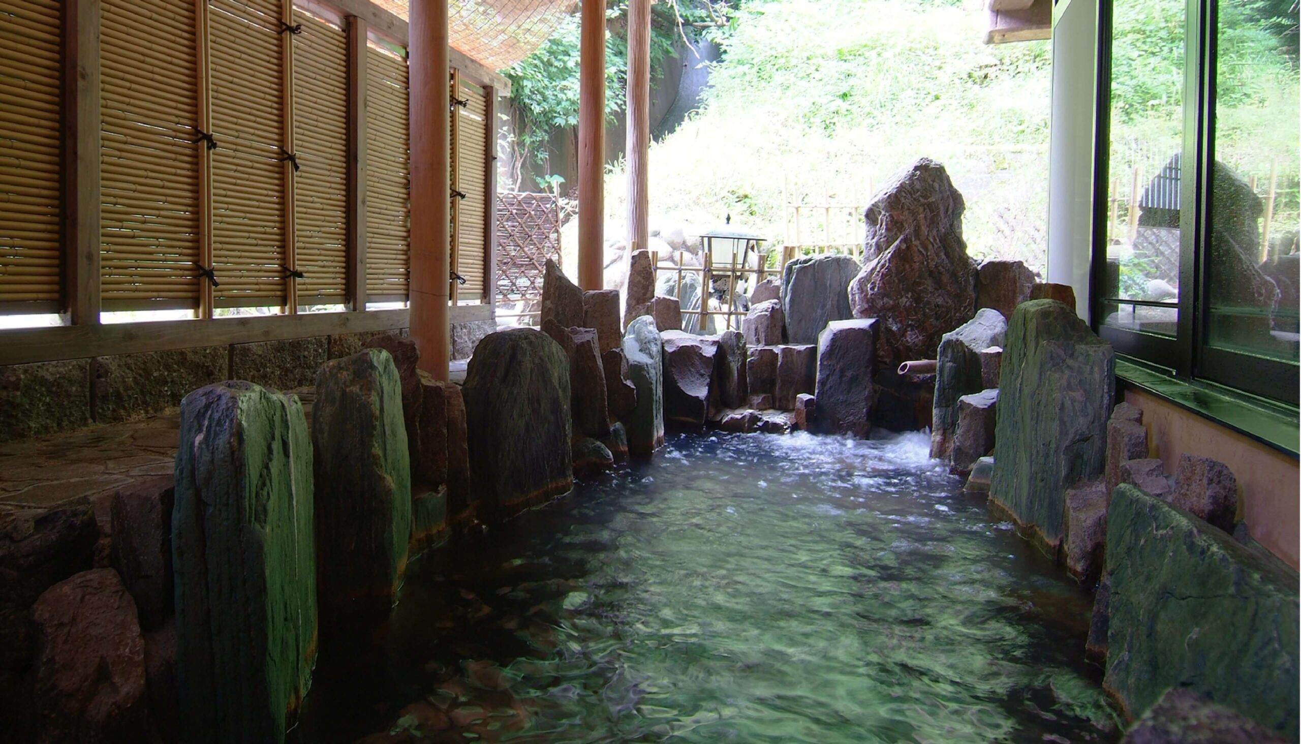 民芸味の宿 白川屋 — 新潟県十日町市松之山湯本 · 石組みに囲まれた露天風呂と竹垣、湯面に映る緑