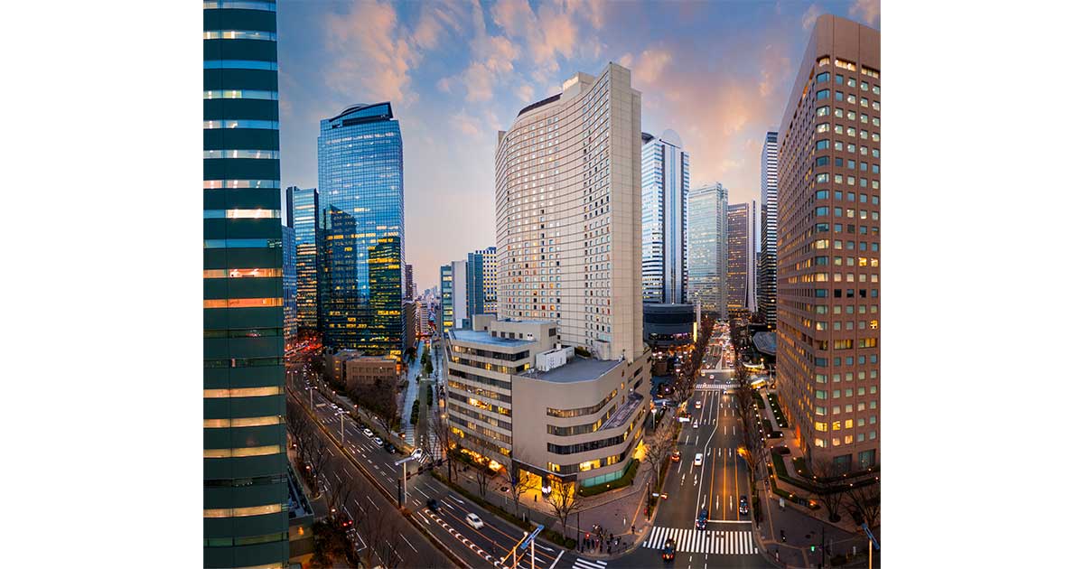 ヒルトン東京 — 東京・西新宿 · 高層ビル街の通り沿いに建つ曲面の外観と夕景の街並み
