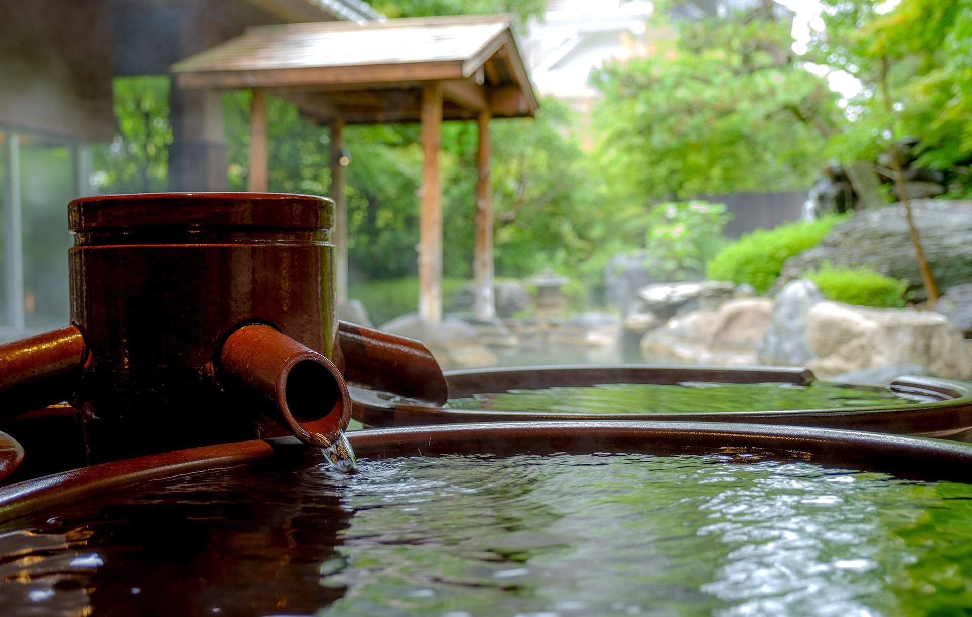 三朝館 — 三朝温泉 · 庭園風呂に置かれた陶器の壺湯と源泉の注ぎ口