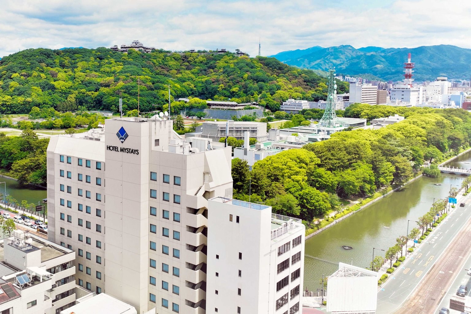 ホテルマイステイズ松山 — 松山市大手町 · 堀端の緑と松山城の山を背にした白い外観