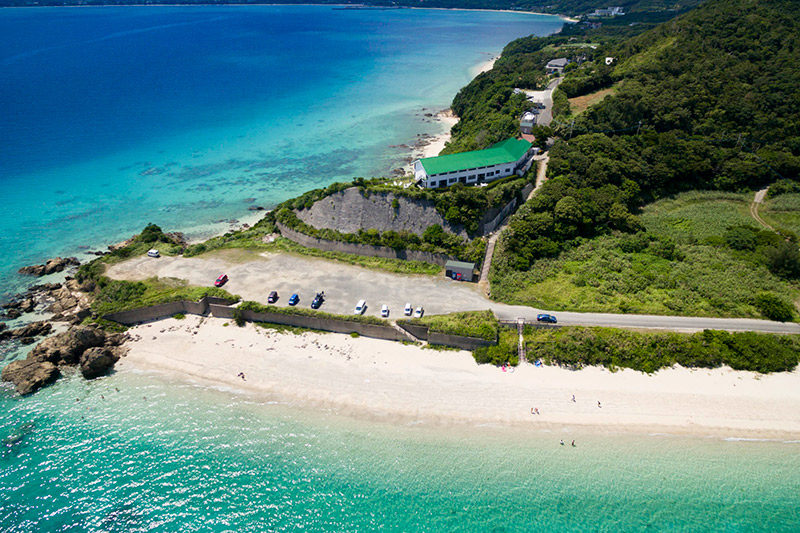 プチリゾート ネイティブシー奄美 — 龍郷町芦徳 · 海沿いの高台に建つホテルと前の砂浜の空撮